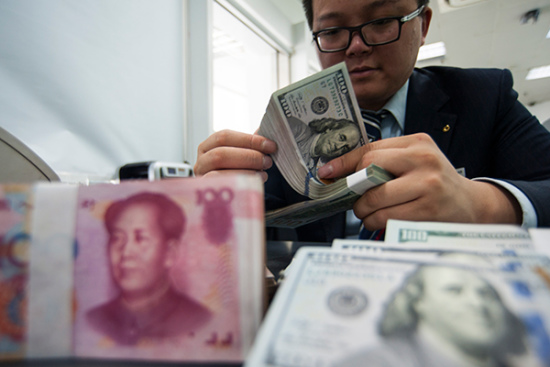 An employee at a bank counter in Nantong, Jiangsu province, counts renminbi and dollars. [Photo/China Daily]