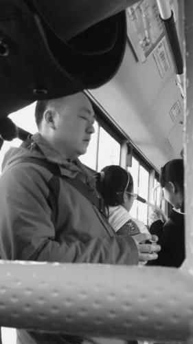 the photo shows a man, lying against a handrail, twisted the Rubik's Cube on a bus of Shenyang, with eyes closed, 