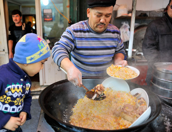 A Uygur child cannot wait to have the pilaf for lunch. [Photo by Han Liang/For China Daily]  