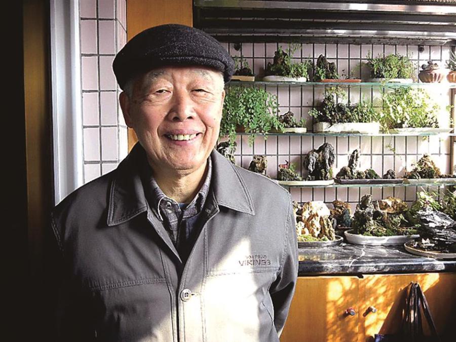 Ma Boqin and his bonsai. (Photo/Shine.cn)

Ma Boqin, 84, is a gardener who doesn’t need water. For almost a quarter-century, he has made a hobby of miniascapes, or dish gardens with dry or other plant materials that don’t require water.

He has exhibited his works around Shanghai.

“Money isn\'t my biggest concern,” said Ma. “The happiness my hobby brings me is more important.”
The Minhang resident first discovered this form of bonsai when he retired at age 60. He immediately fell in love with the art form and joined the Shanghai Miniascape Association.

The genre traces its roots in China back about 1,000 years ago. It is said to have been initially inspired by the beauty of short, twisted trees rooted on cliffsides. Later, the concept went on to form the basis of Japanese bonsai.

“It\'s a miniature of natural scenery in a pot,” Ma said of bonsai, “but as the art form evolved, it focused only on plants, losing its artistic essence.”

Ma turned his hand to traditional bonsai but found he wasn’t particularly good at it.

“In a hot summer like this one, you need to water bonsai twice a day,” he said. “I felt tied to the plants. I couldn’t leave home for long. It’s a hobby for people who have time.”

So Ma gave up traditional bonsai and turned to a more modern version. He uses tree trunks, rocks and other materials of nature to re-create scenery or scenes from traditional paintings and poems.

“I think miniascape suits modern life better,” he said.

Traditional bonsai done for exhibitions, he said, often involves pruning just a few days before an event. After the show, the plants are left to die in their pots. At best, a bonsai can survive for no more than 100 years, he said.

“My works can be kept forever,” he explained.

Ma has re-created scenes from 300 Tang Dynasty (AD618-907) poems based on how the verse stirred his imagination. His miniascape works can be divided into more than 11 categories by themes and styles. Not all are traditional.

“I created miniascapes about line dancing,” he said. “And when the country called for people to join the army, I created a scene from ‘Mulan Joins the Army.’”