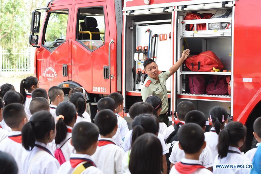 A fire fighter introduces fire-fighting equipments to pupils from Chengguan No.1 Primary School in Yuqing County of Zunyi City, southwest China\'s Guizhou Province, Aug. 27, 2018. Pupils from Chengguan No. 1 Primary School learnt knowledge of fire-fighting at the first day of the new semester. (Xinhua/He Chunyu)