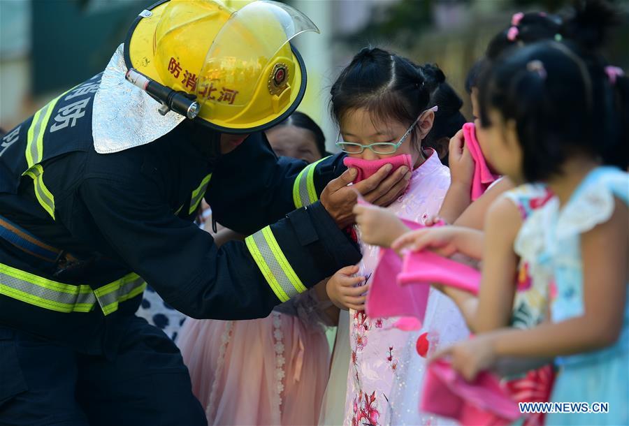 A fire fighter instructs children to escape in a drill of fire emergency at Xinhua District of Cangzhou City, north China\'s Hebei Province, Aug. 27, 2018. Children and students at Xinhua District participated in a drill of fire emergency before the new semester. (Xinhua/Fu Xinchun)