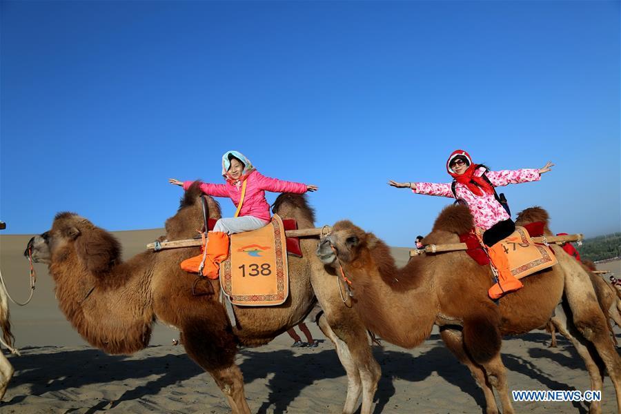People ride camels at the Crescent Moon Spring scenic spot on the Mingsha Mountain in Dunhuang, northwest China\'s Gansu Province, Oct. 3, 2018, the third day of the week-long National Day holiday. (Xinhua/Zhang Xiaoliang)