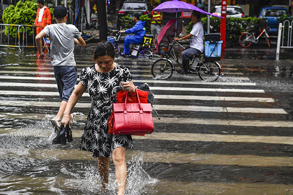 People walk across a flooded street in Guangzhou, Guangdong province, on Monday. Kindergartens and primary and middle schools were closed after Typhoon Mawar battered the city.(Photo/Chinanews.com)