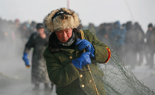 Fishermen drill circular holes in the ice on the lake. Then they hook and pull the fishing net through the holes to create a net under the thick ice.[Photos by Bai Shi / For China Daily]