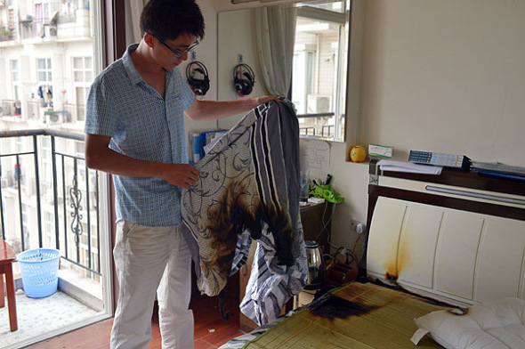 Wang Kai shows his burnt sheet and mat after his iPhone 4 exploded in Chongqing, on July 9, 2013. [Photo by Yu Xiao/Asianewsphoto]