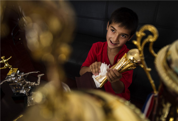 A ten-year-old member of the Urumqi Fifth Primary School soccer team wipes a trophy in the team's trophy room on Aug 12 in Urumqi, Xinjiang Uygur autonomous region. [Photo/Xinhua]