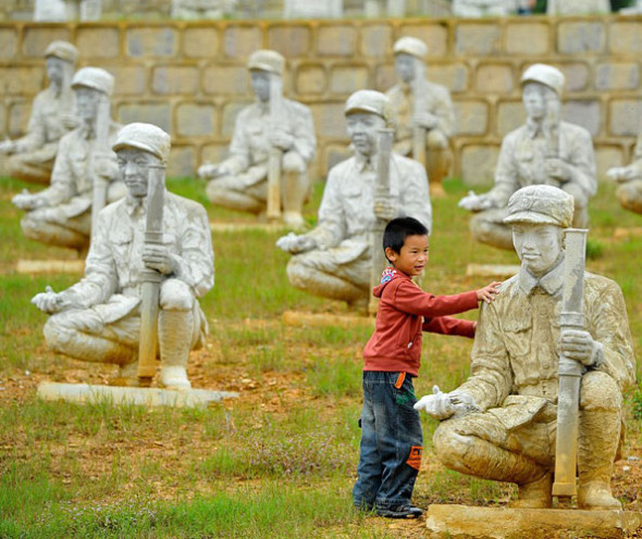 A child poses with sculptures of soldiers from the Chinese Expeditionary Force, which helped defeat Japanese forces during the conflict, on Songshan Mountain, Longling county, Yunnan province, Sept 3, 2013. [Photo by Chinanews]