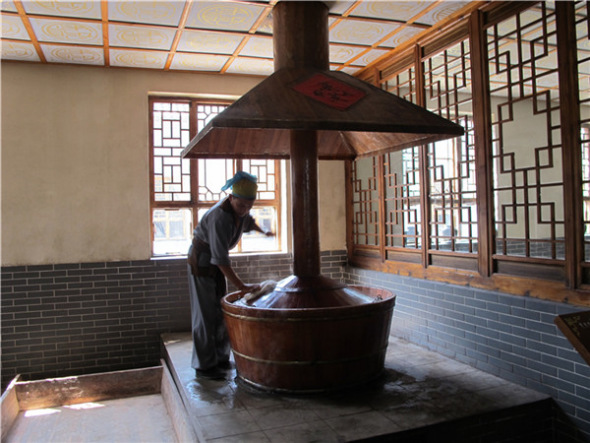 A worker dressed in ancient costume is braising ingredients for vinegar at Baoyuan Vinegar Workshop in Qingxu county, North China's Shanxi province, Sept 5, 2013. [Photo by Guo Rong/chinadaily.com.cn]