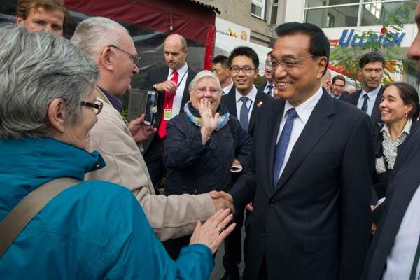 Premier Li Keqiang, accompanied by German Chancellor Angela Merkel, greets local residents on a street in Berlin on Oct 10, 2014. [Photo/Xinhua]