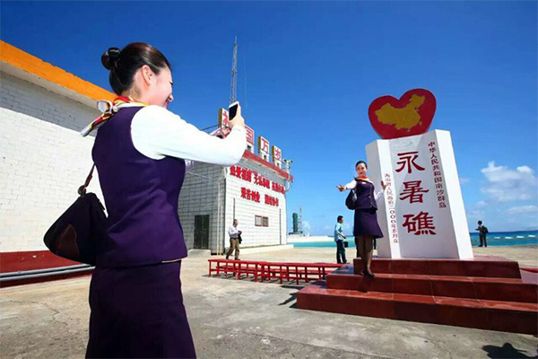 A stewardess takes a photo standing beside a monument with Chinese characters of Yongshu Jiao inscribed on it. (Photo/Xinhua)